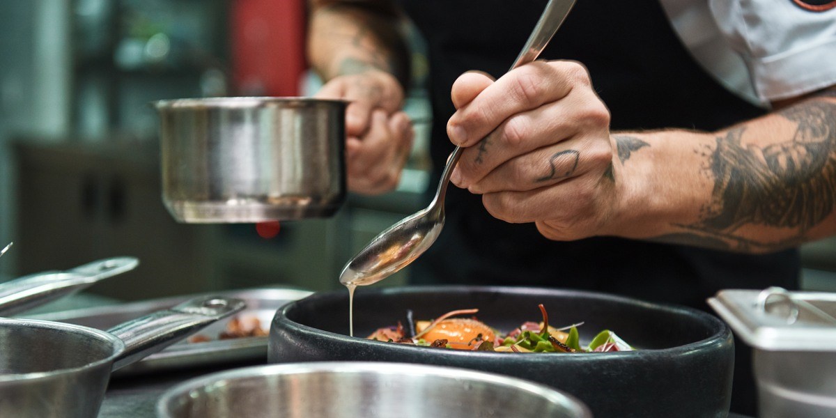 Secret recipe. Close up photo of chef hands with several tattoos adding a sauce to italian pasta Carbonara. Food concept